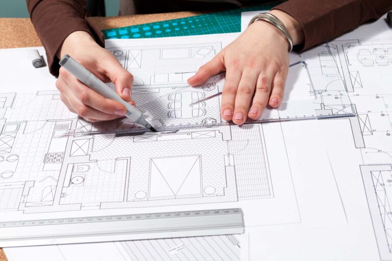 Architect reviewing structural floor plans and drafting architectural drawings at a desk.*